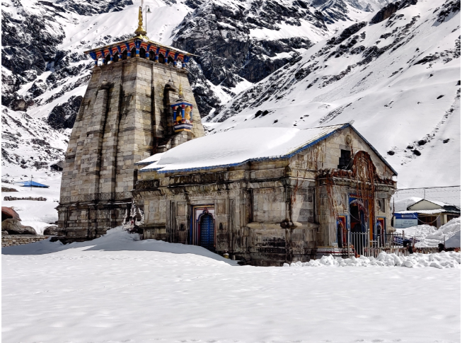 Ancient stone structure of Kedarnath Temple covered in snow with mountains behind it